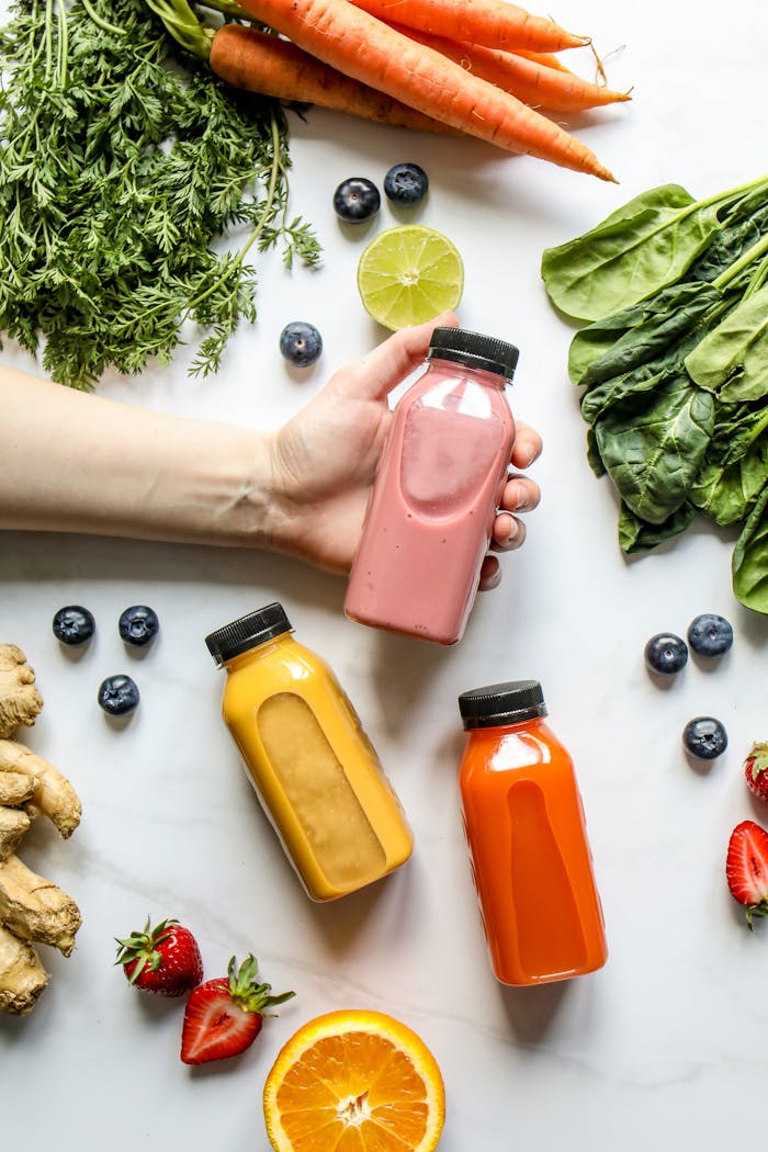 Person Holding Bottle of Smoothie Beside Green Leaves, Carrots and Berries